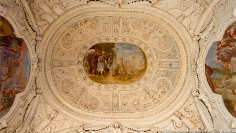 Oval figurative fresco centered within an elaborate circular white stucco ceiling frame.