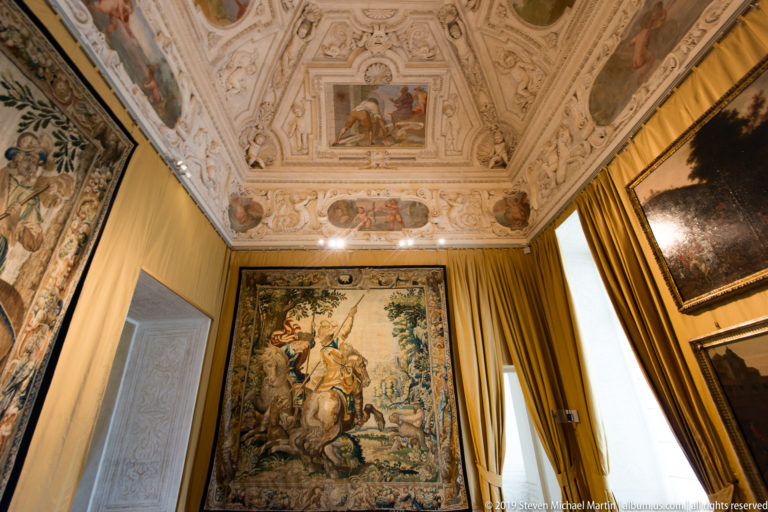 Tapestry room with a large hunting tapestry, gold curtains, and an elaborately frescoed and stuccoed ceiling.