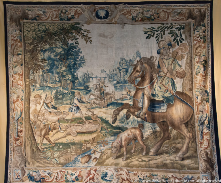 Tapestry of a mounted hunter with dogs in the foreground and additional riders across a distant landscape.