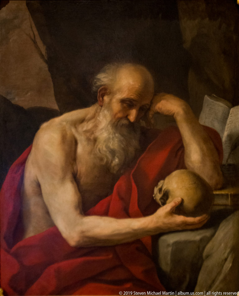 Painting of an elderly bearded saint in a red mantle contemplating a skull beside a book.