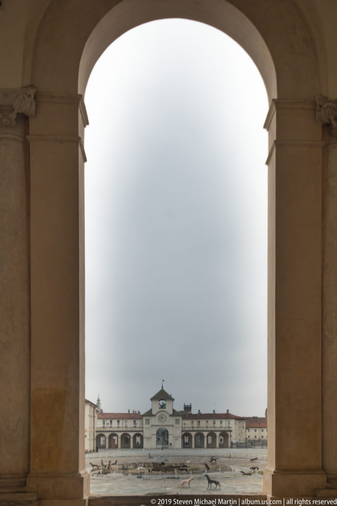 Distant pale palace building centered beneath a large stone archway across an open courtyard.
