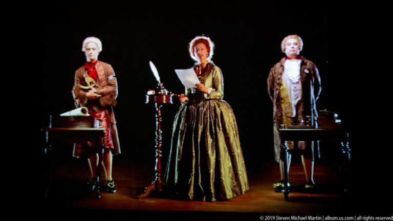 Three period-costumed figures reading and writing at tables in Peter Greenaway’s Ripopolare la Reggia installation.