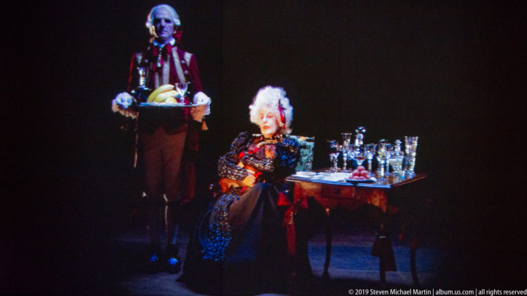 Projected courtly woman at a laden table with a liveried servant in Peter Greenaway’s Ripopolare la Reggia installation.