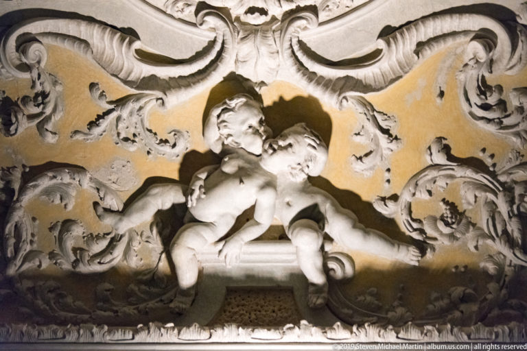 Two stucco putti seated among deep scrolling foliage and shell-like ceiling ornament.