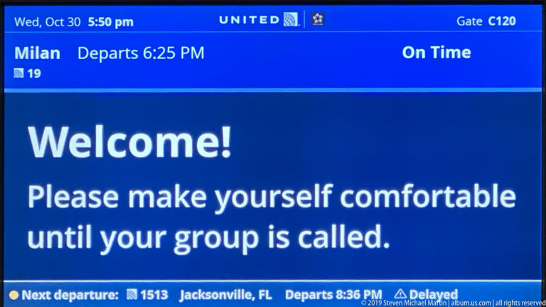 Blue United Airlines gate screen showing a welcome message, Gate C120, on-time status, and boarding information.