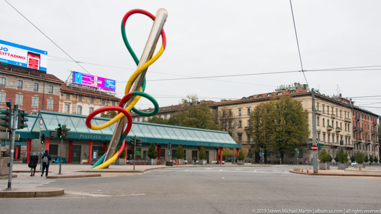 Large red, green, and yellow Needle, Thread and Knot sculpture rising in Piazzale Cadorna, Milan.