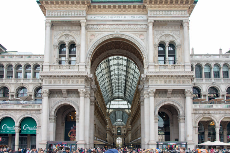 Grand arched entrance to the Galleria Vittorio Emanuele II from Piazza del Duomo, with crowds below the glass-roofed passage.