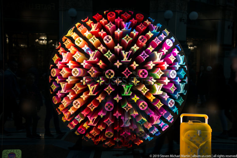 Colorful illuminated Louis Vuitton monogram forms arranged as a sphere in a dark Milan shop window.