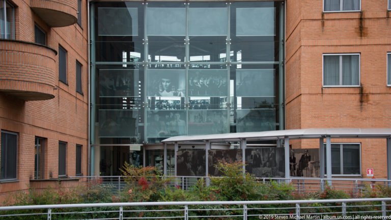 Modern red-brick building with a tall glass entrance volume and black-and-white photographic panels.