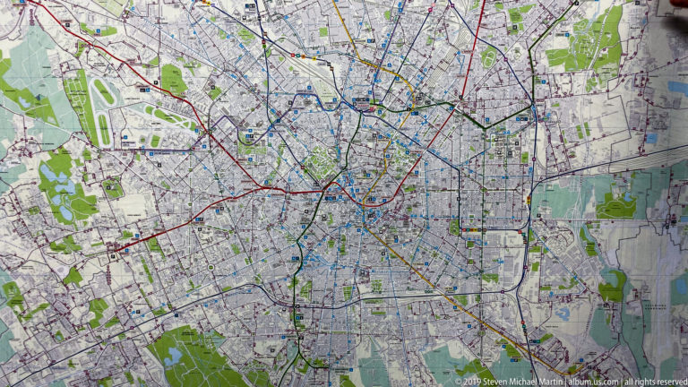 Large printed map of Milan showing streets, parks, railways, waterways, and colored transport routes.