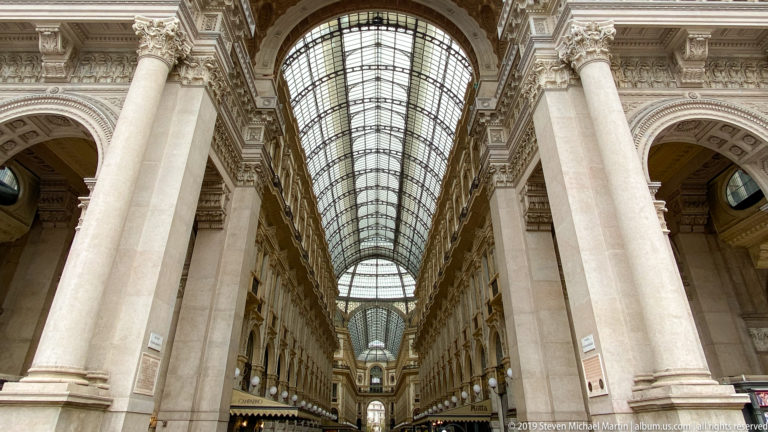 Tall stone columns framing a long glass-roofed passage inside the Galleria Vittorio Emanuele II.