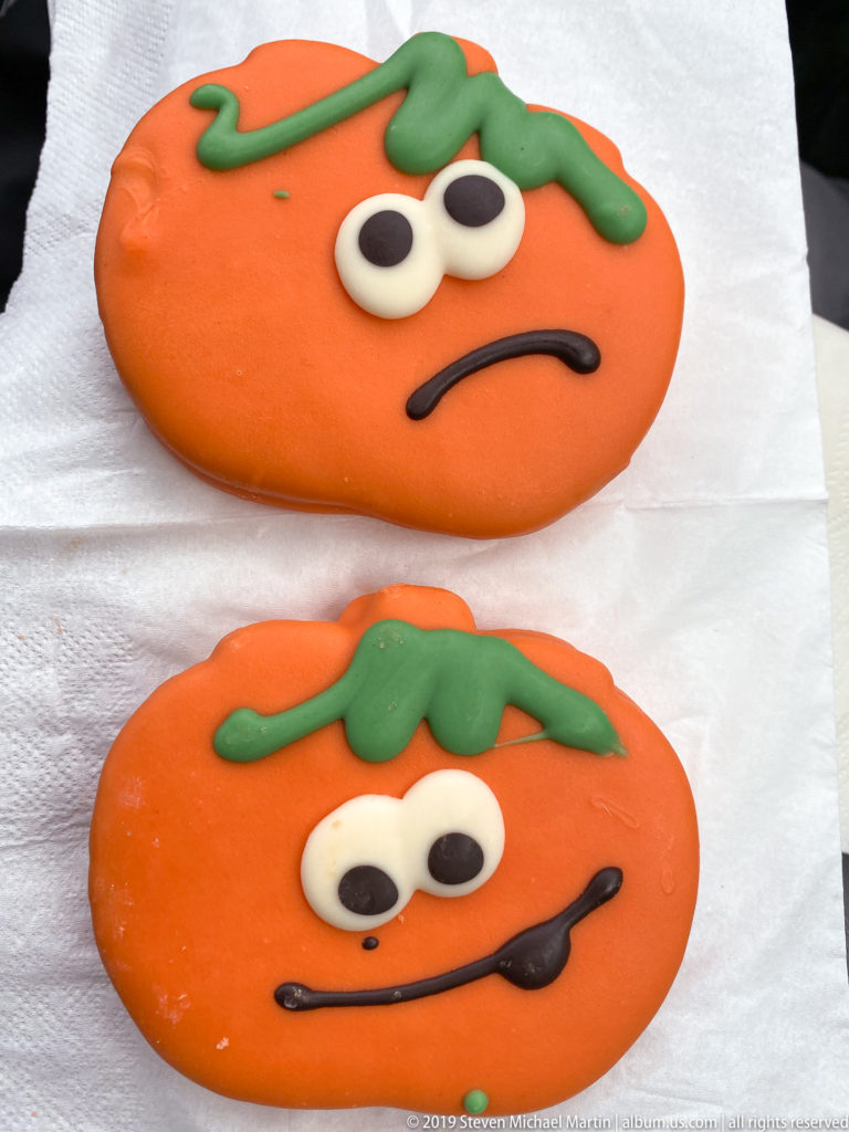 Two orange tomato-shaped iced pastries with green leaves, cartoon eyes, and contrasting facial expressions.