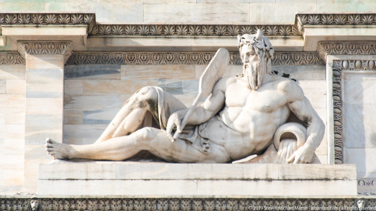 Reclining bearded marble river-god figure with an oar on the Arco della Pace.