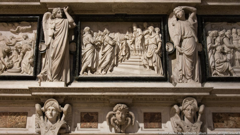 Carved marble monument with a central narrative relief, standing figures, side panels, and sculpted heads along the lower frame.