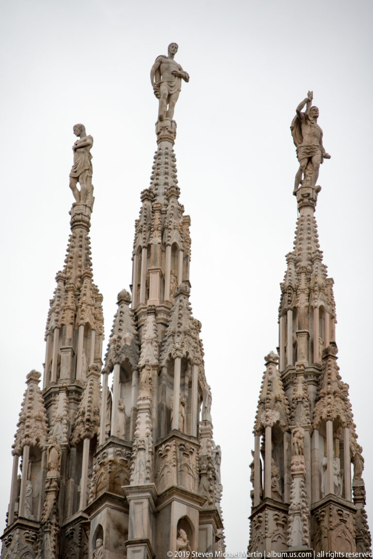 Three ornate Gothic rooftop spires with open carved stages, crockets, and sculptural figures at their summits.