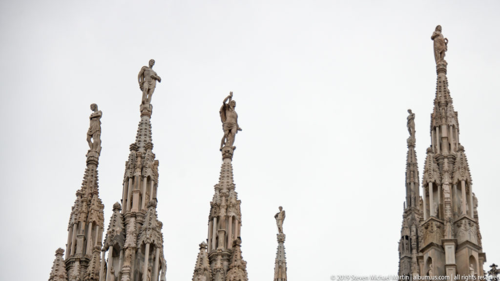 Cluster of ornate Gothic pinnacles of different heights, each crowned by a standing stone statue against the sky.