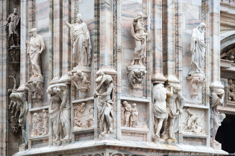 Several adjacent marble façade bays filled with standing statues, crouching figures, narrative reliefs, masks, and carved borders.