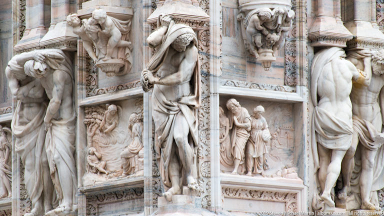 Close façade bay with bowed supporting figures, small narrative reliefs, projecting brackets, and narrow carved borders.