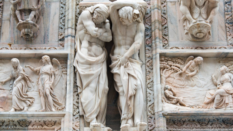 Two bowed marble supporting figures centered between narrative relief panels, masks, and carved ornamental bands.