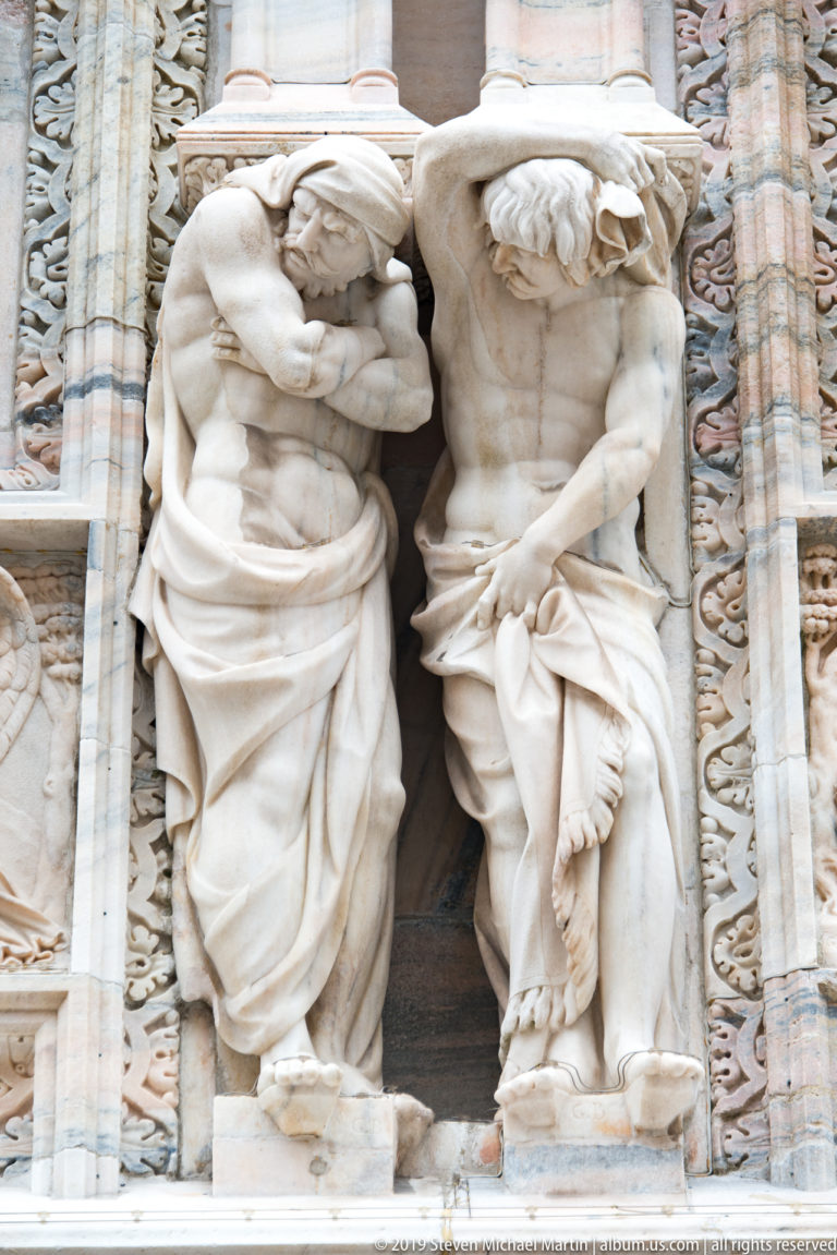 Two marble supporting figures bent beneath projecting ledges, with contrasting drapery and muscular poses on the façade.