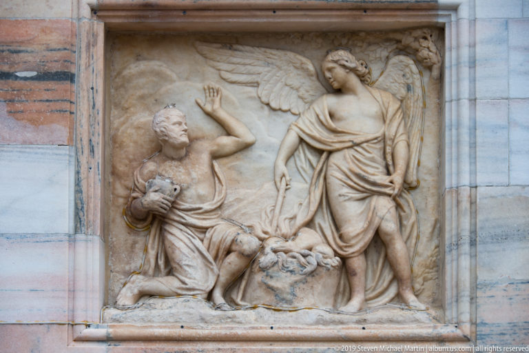 Winged marble figure facing a kneeling man with one raised hand in a shallow rectangular narrative relief.