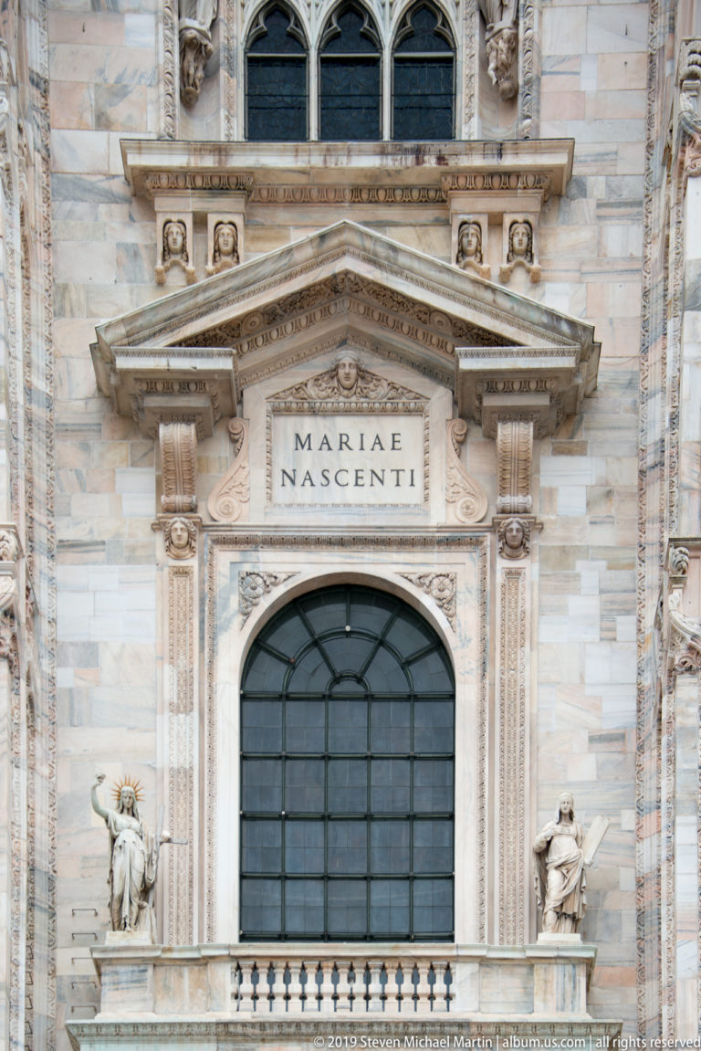 West façade bay with MARIAE NASCENTI inscription above an arched window, flanked by statues and carved marble architecture.