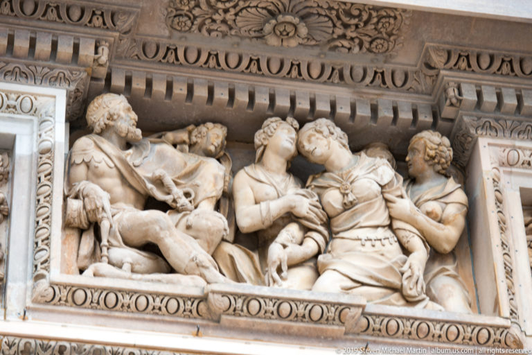 Close marble relief of a reclining figure surrounded by three attendants within a richly molded rectangular frame.