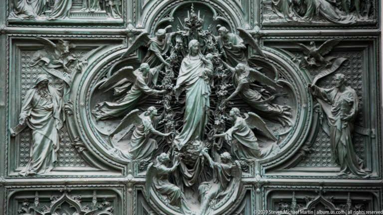 Central bronze oval relief with a standing sacred figure, kneeling attendants, angels, and flanking figures.