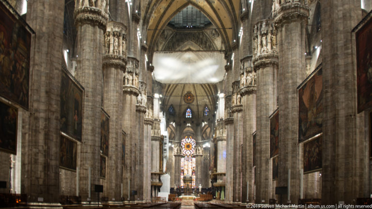 Vertical nave view between towering clustered piers, with large paintings and stained glass visible in the distance.