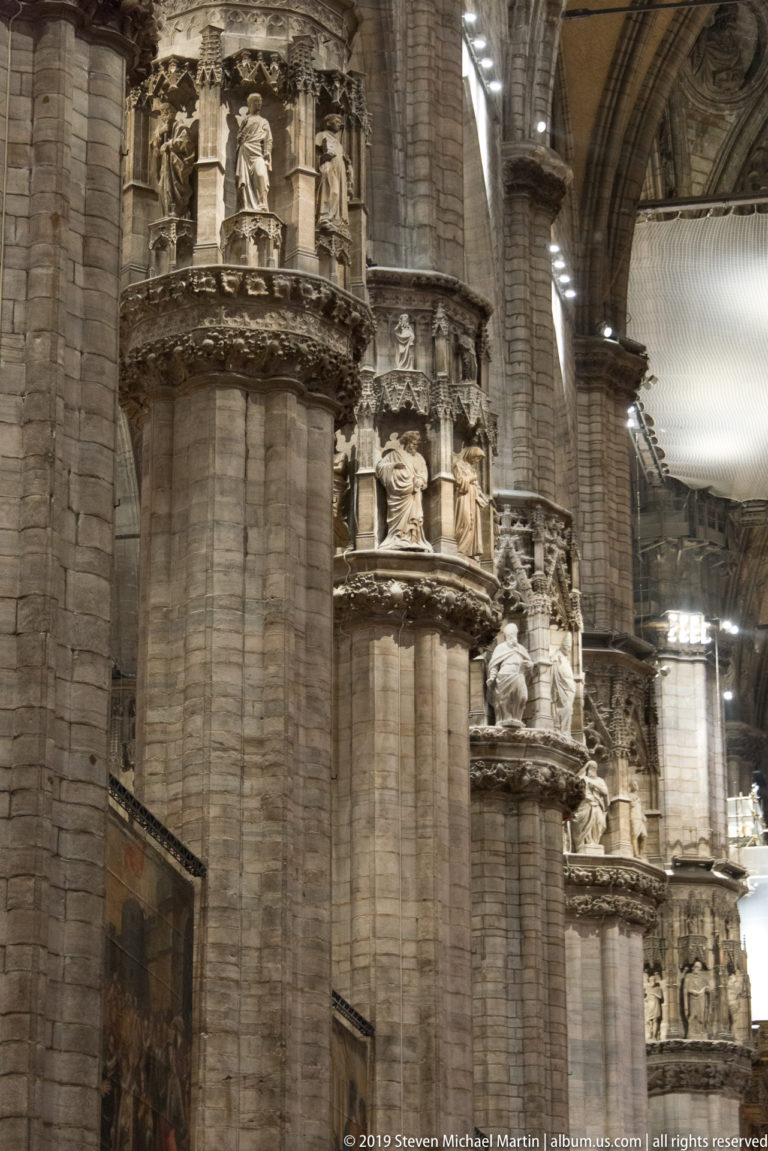 Row of massive cathedral piers with repeating sculpted capitals beneath pointed arches and high Gothic vaults.