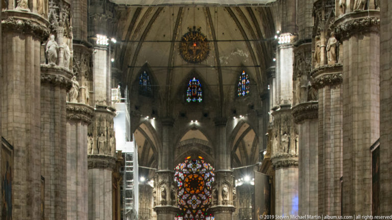 Tall Gothic interior with clustered piers, sculpted capitals, pointed vaults, and stained-glass windows at the far end.