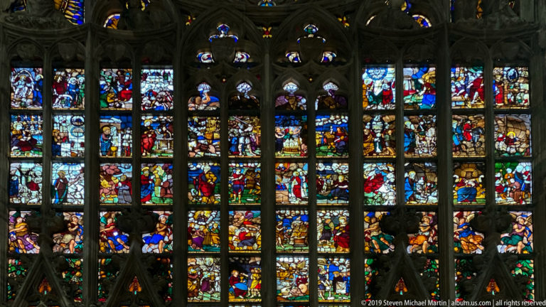 Colorful biblical figures and scenes fill stacked stained-glass panels divided by dark Gothic mullions and tracery.