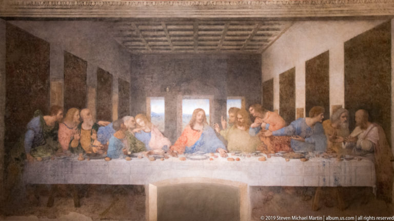 Full frontal view of The Last Supper with Christ centered, twelve apostles at the table, and a doorway cut below the central figure.
