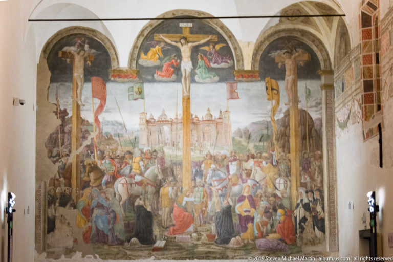Full Montorfano Crucifixion viewed from within the refectory, framed by pale walls and the surrounding architecture.