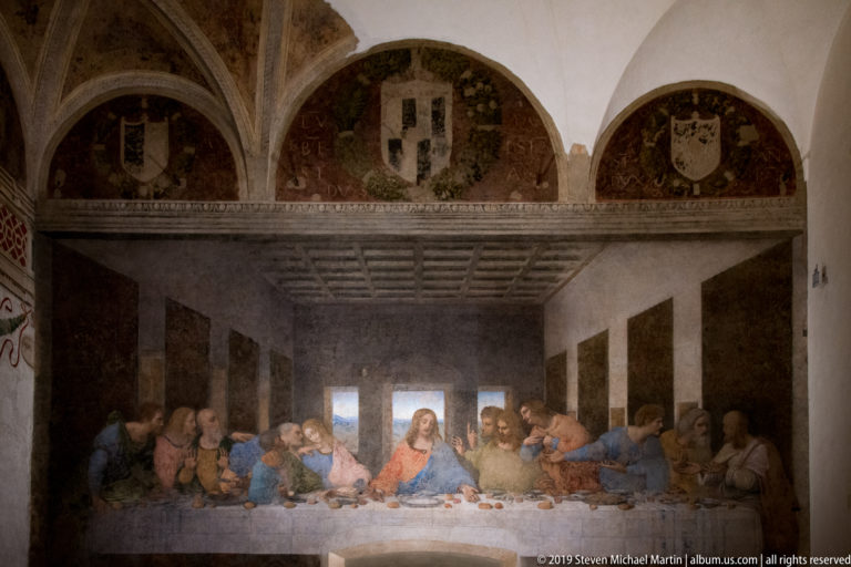 Full view of The Last Supper beneath three faded heraldic lunettes on the north wall of the refectory.