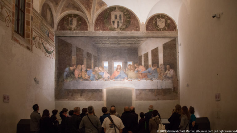 Visitors gathered before Leonardo’s The Last Supper beneath three decorated lunettes in the Santa Maria delle Grazie refectory.