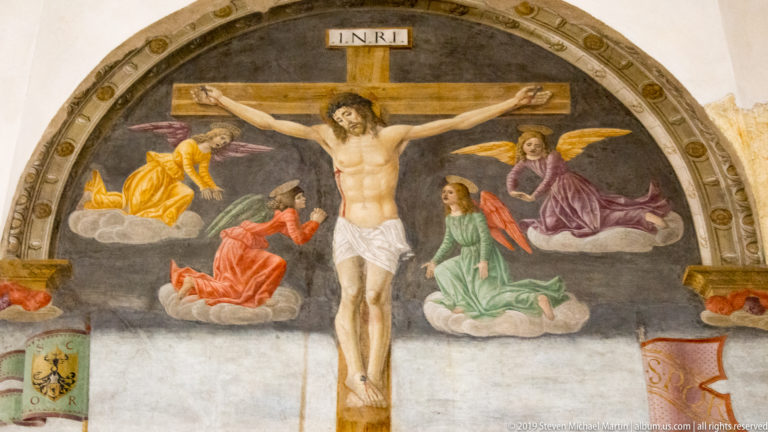 Close detail of the crucified Christ beneath INRI, with four colorful angels arranged on clouds around the cross.