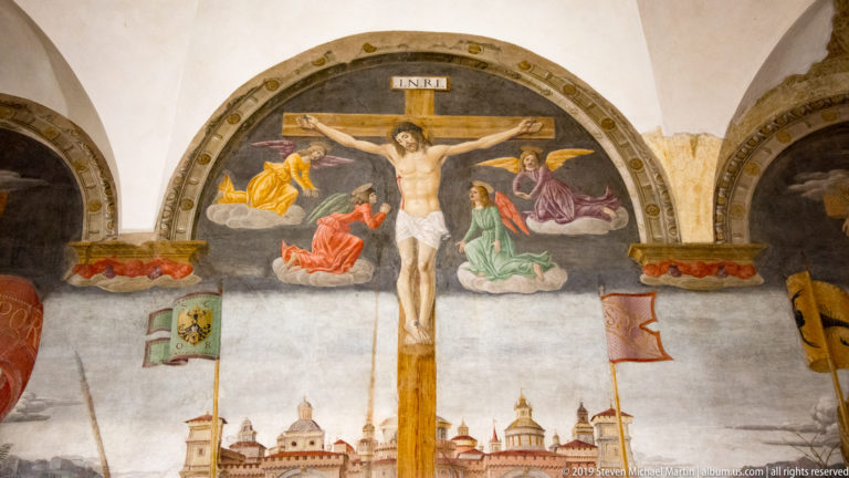 Christ on the central cross beneath an INRI tablet, surrounded by angels above the Jerusalem background.