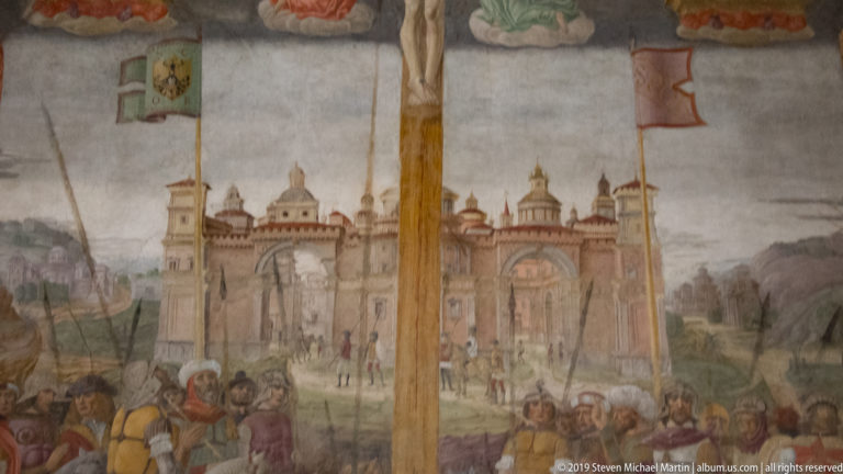 Painted Jerusalem with towers and domes behind a crowd, flanked by two banners beneath the central cross.