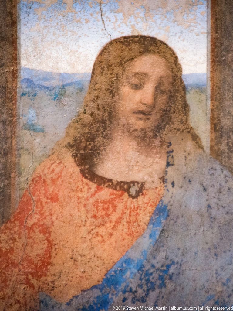 Close detail of Christ’s face and red-and-blue garments at the center of Leonardo’s The Last Supper, with extensive surface loss.