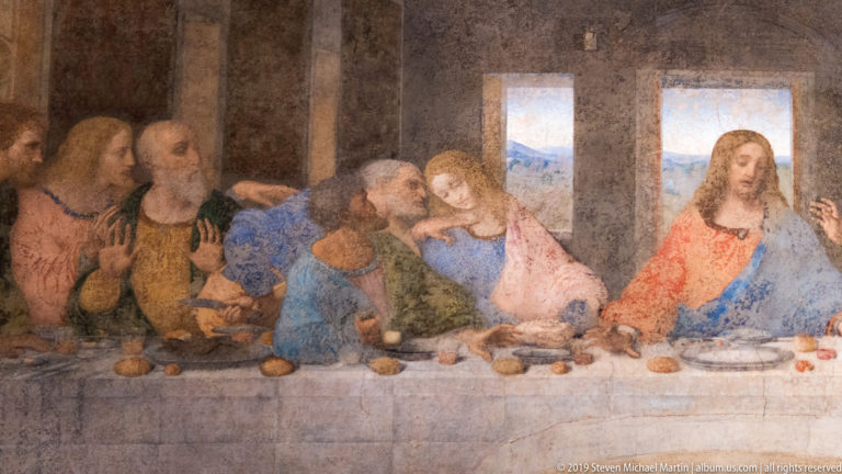 Apostles on the right half of The Last Supper gesture across the table, with blue landscape visible through two windows.