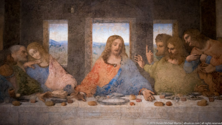 Christ centered before a bright window in The Last Supper, with apostles leaning and gesturing on both sides.