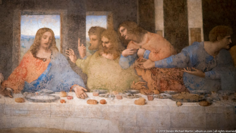 Christ in red and blue beside three gesturing apostles at the table in Leonardo’s The Last Supper.