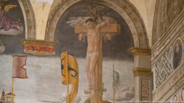 Crucified figure in a dark arched field above painted standards and decorative borders in Montorfano’s Crucifixion.