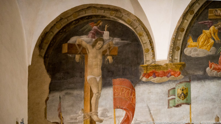 Crucified figure against a dark arched background above colorful military banners in Montorfano’s Crucifixion.