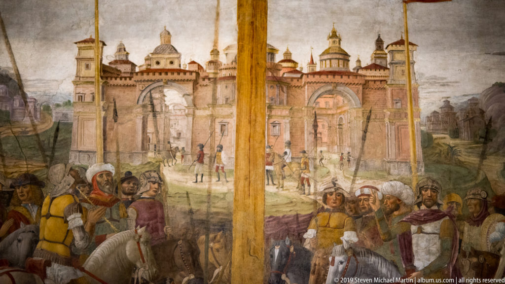 Painted Jerusalem with towers, domes, gates, and walls behind soldiers gathered beneath a tall cross in Montorfano’s Crucifixion.