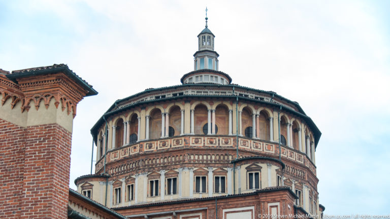 Close view of the Santa Maria delle Grazie tribune with an arcaded upper drum, patterned brickwork, pale panels, and lantern.