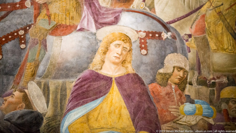 Haloed mourning woman in purple and yellow surrounded by soldiers, weapons, and standards in Montorfano’s Crucifixion fresco.