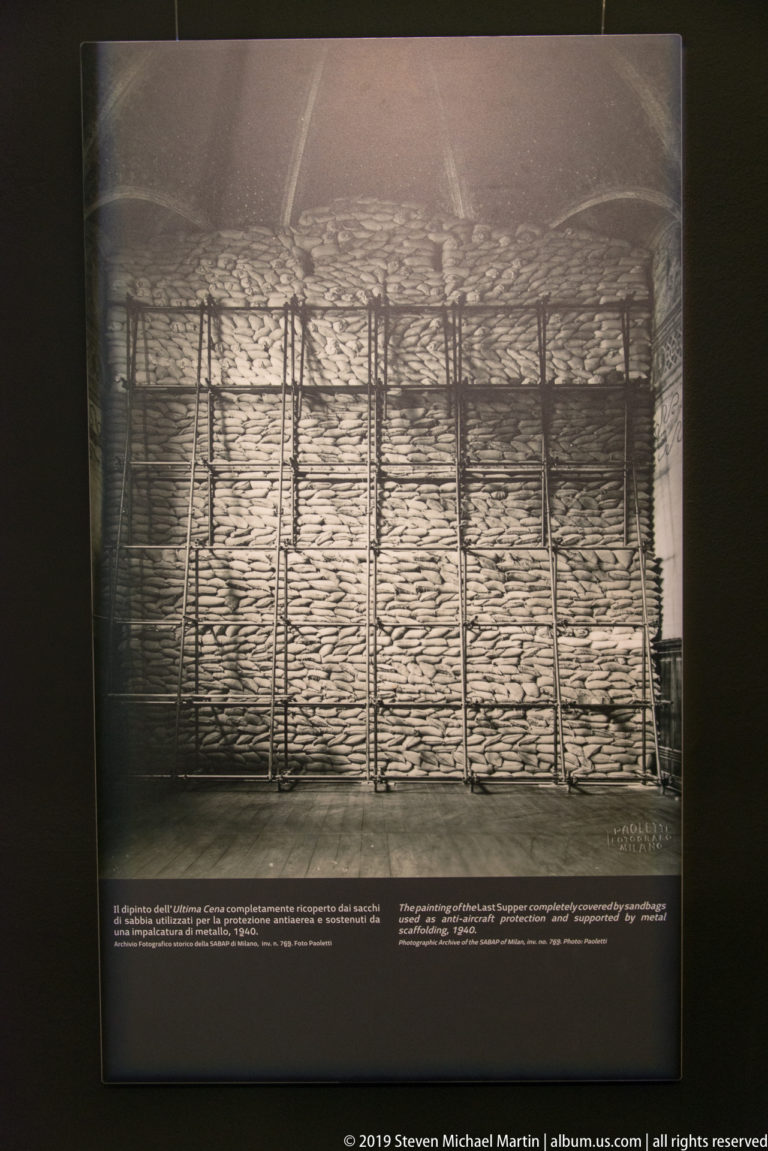 Archival museum display showing dense sandbagging and scaffolding erected across the wall of The Last Supper during World War II.