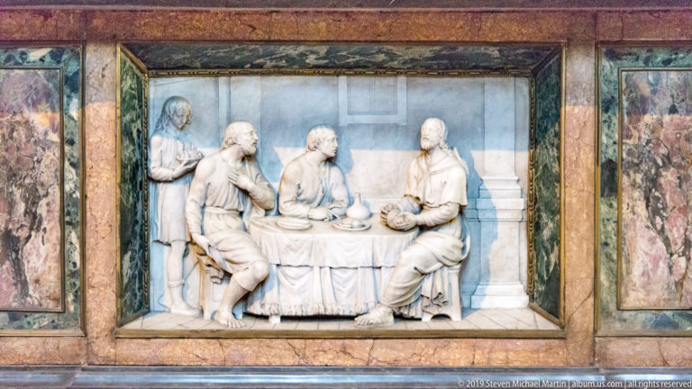 White marble relief of Christ and apostles seated around a table, framed by panels of colored marble.